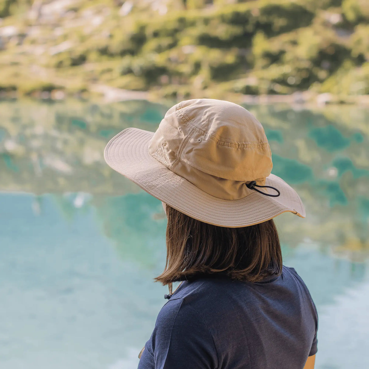 Frau mit Sonnenhut von hinten am See, leichter Outdoor Sonnenhut Damen mit breiter Krempe für Wanderungen.
