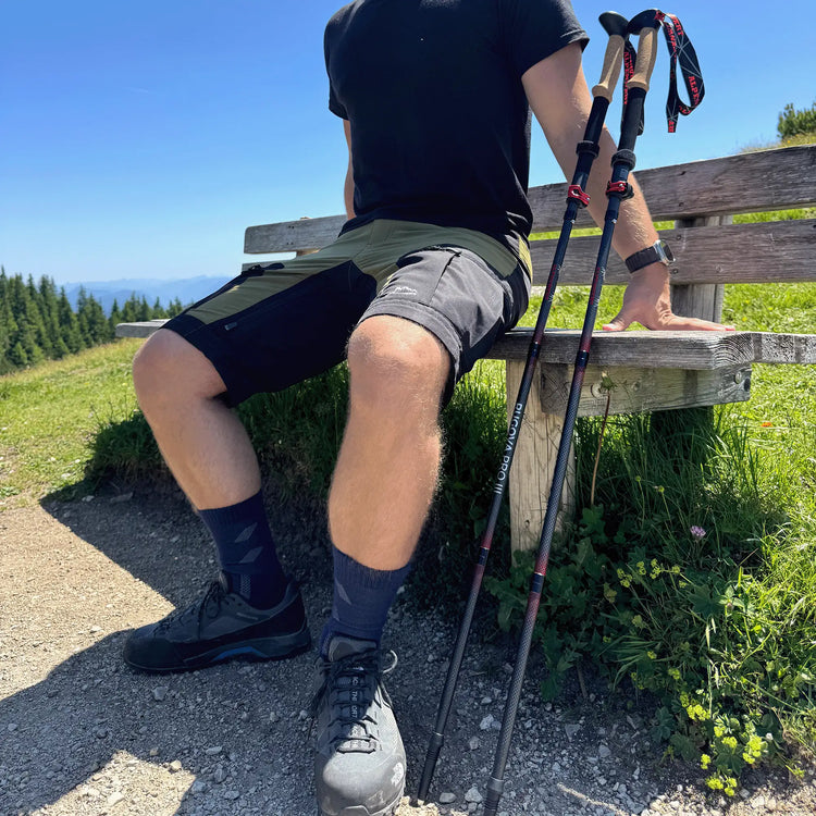 Mann sitzt mit faltbaren Wanderstöcken auf Bank, leichte Trekkingstöcke faltbar für Wanderungen und Bergtouren im Sommer.