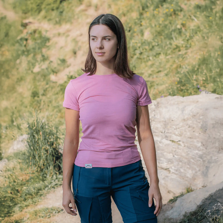 Frau in rosa Merinoshirt Damen vor grüner Natur, funktionales Merino T-Shirt Damen für Outdoor Abenteuer und Alltag.